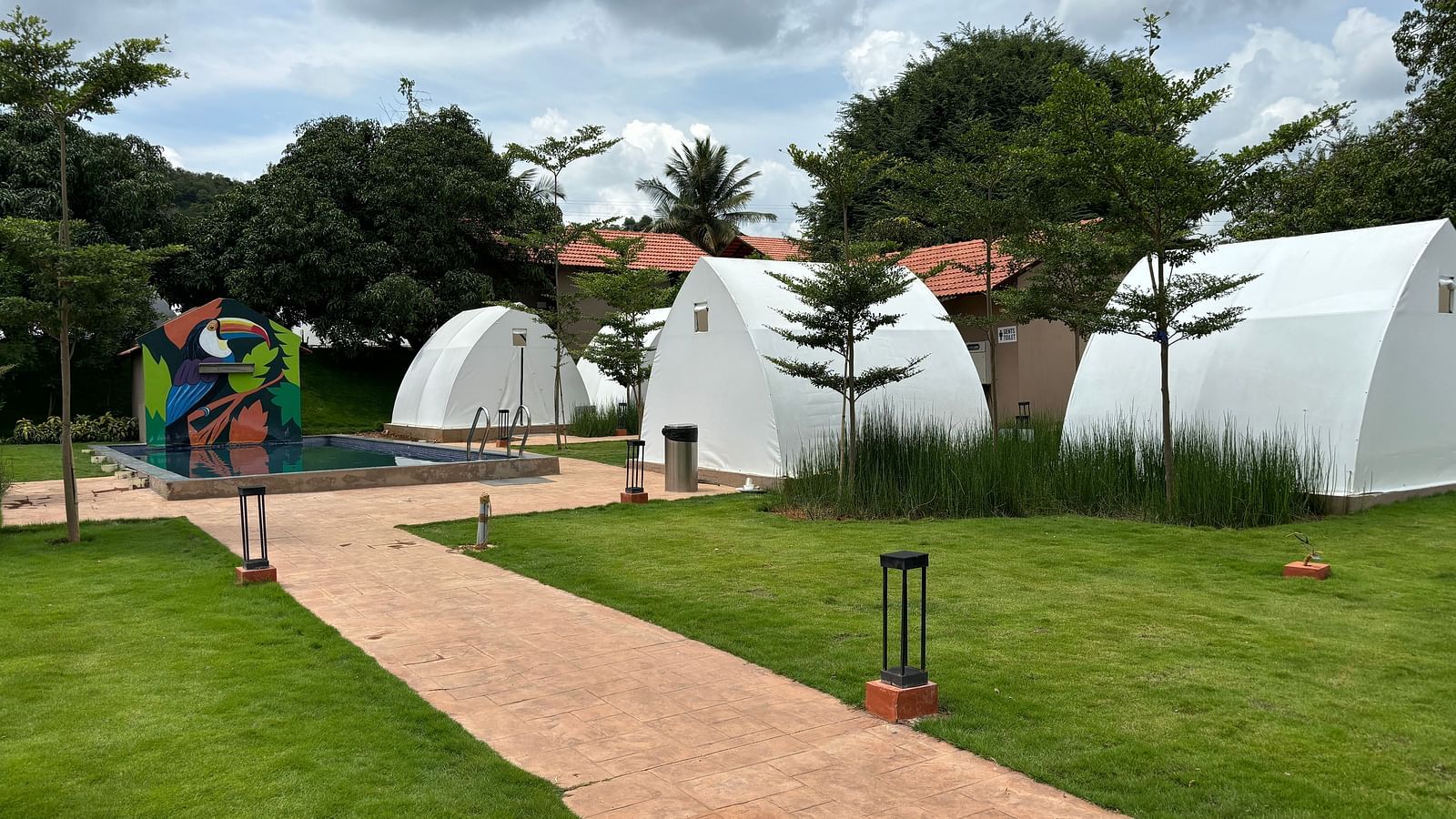 A scenic view of a resort area with tents lined along a neat walkway, surrounded by a well-maintained lawn.