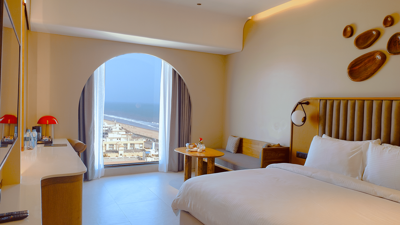 Sea view room with a made bed, an arched doorway leading to a balcony, and a view of the ocean at Swosti Premium Beach Resorts, Puri.