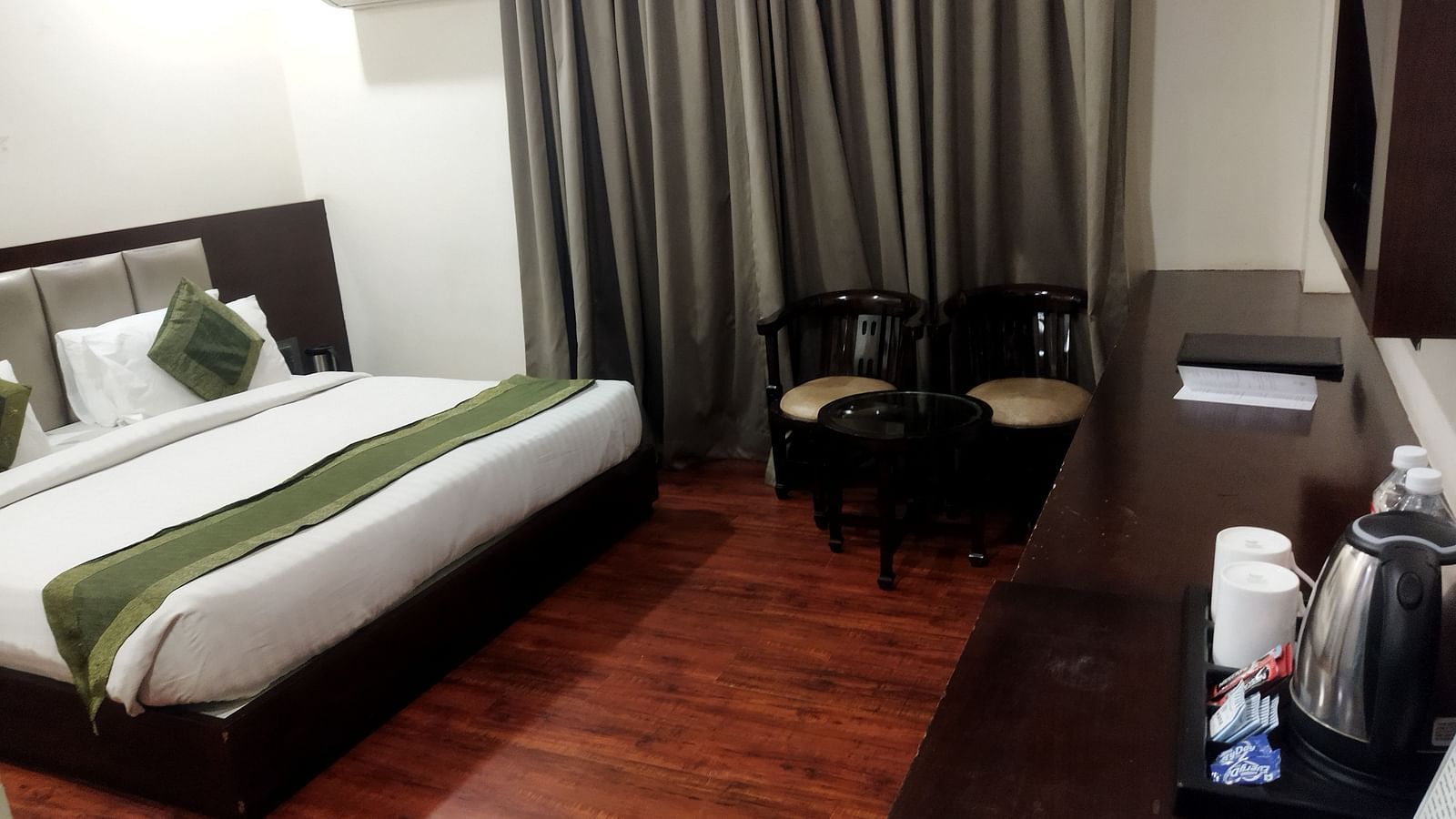A hotel room with a green runner on the bed, a seating area and a long desk with a coffee maker - TGI Apple Inn, Jaipur 