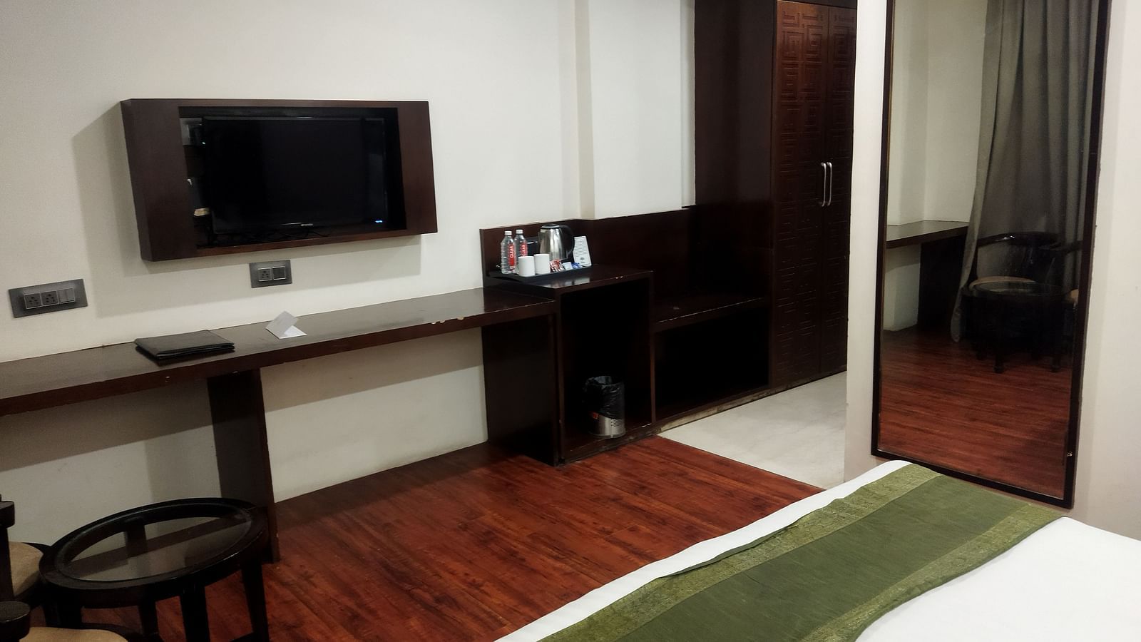A sleek hotel room with a large mirror, a dark wood desk and a bed with a green accent runner - TGI Apple Inn, Jaipur 