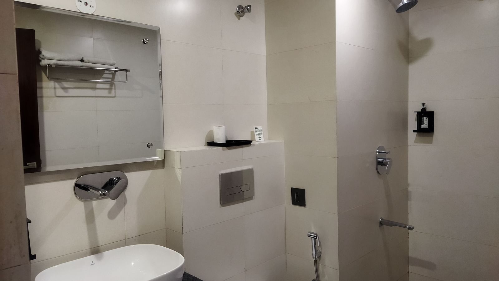 A hotel bathroom with modern fixtures, a wall-mounted sink, a glass shower and beige tiles - TGI Apple Inn, Jaipur 