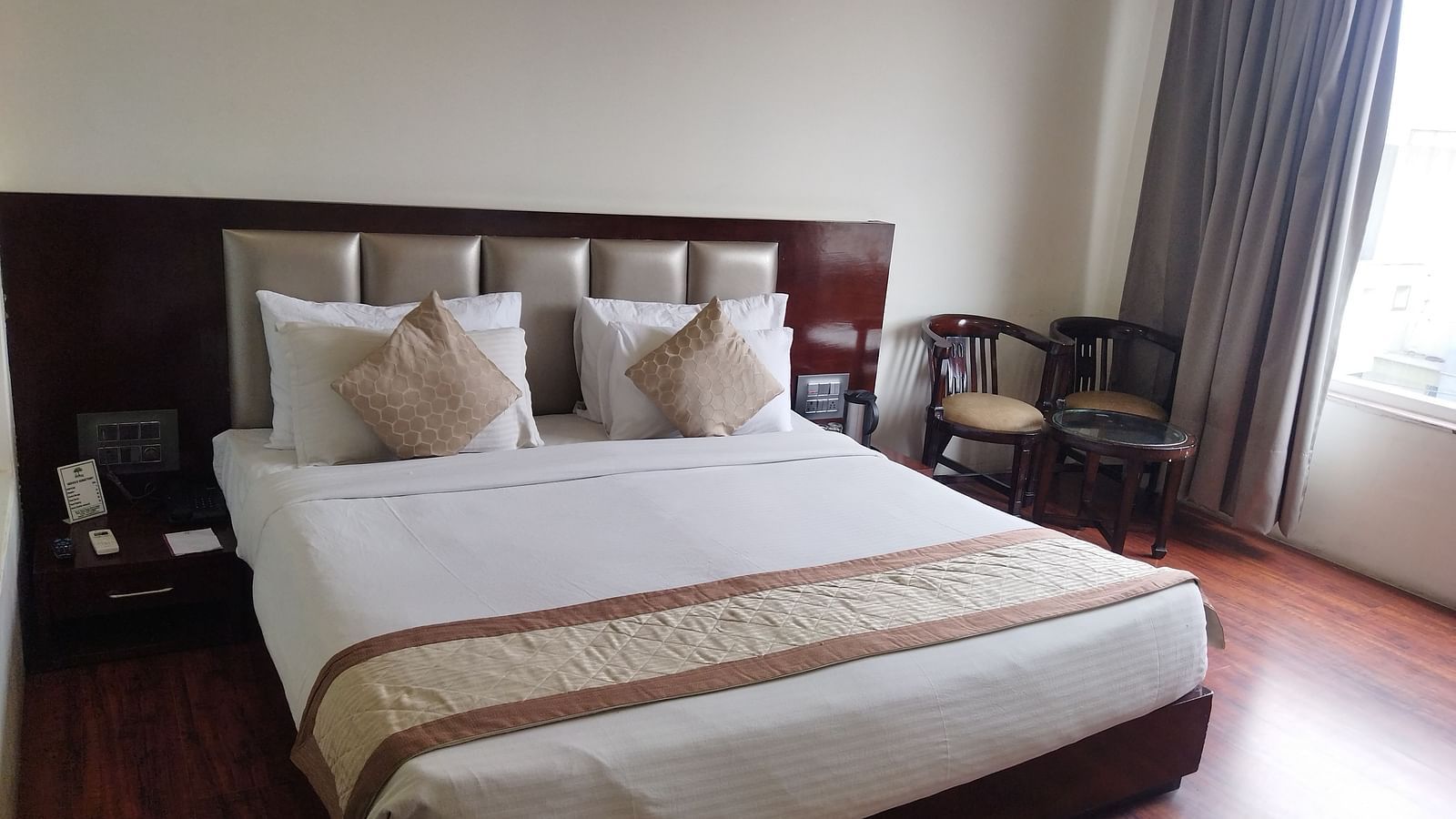 A hotel room with a large bed draped in beige and brown linens and furniture to relax - TGI Apple Inn, Jaipur 