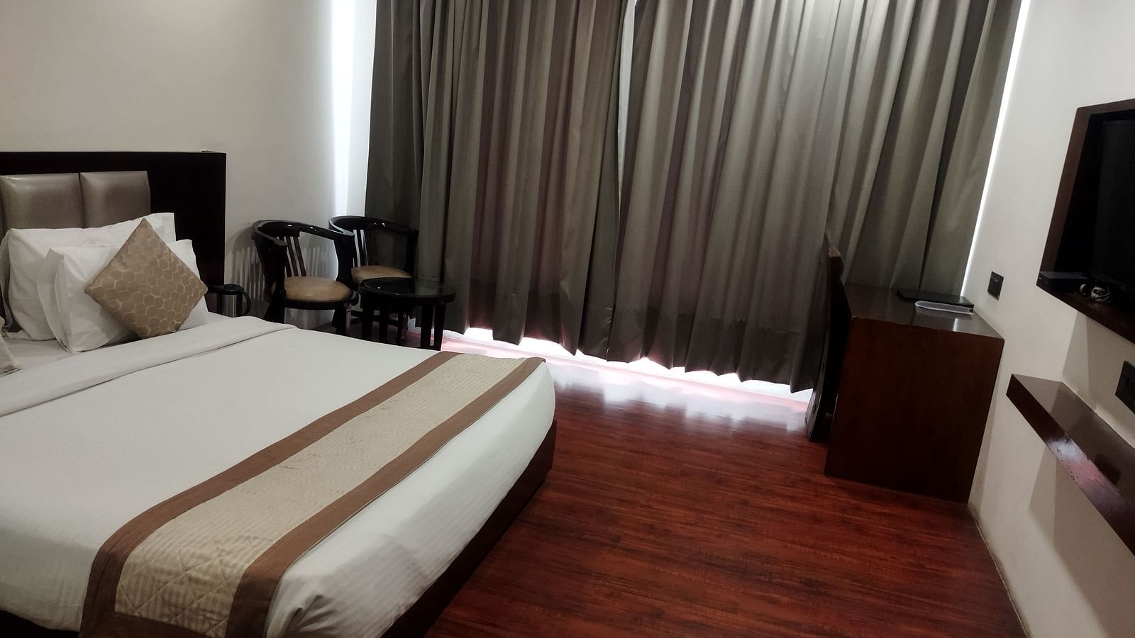 A comfortable hotel room with a large bed draped in beige and brown linens and a flat-screen TV - TGI Apple Inn, Jaipur 