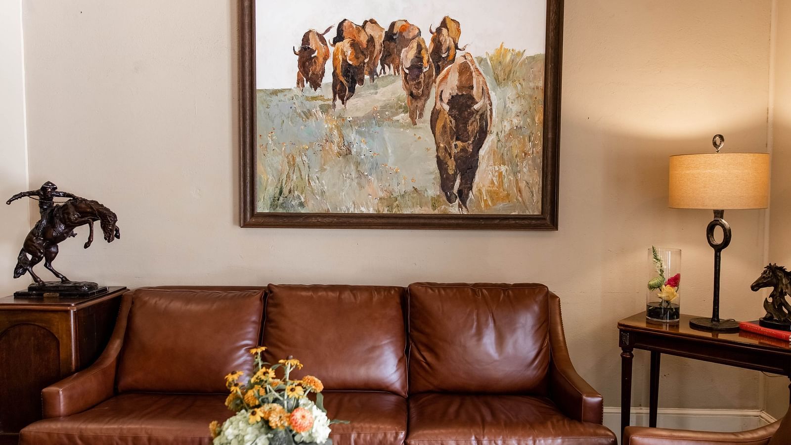 A seating area with a couch, a framed painting , a side table, and a decorative statue.- The Grand Hotel & Ballroom, McKinney