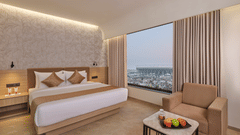 A modern hotel room featuring a king size bed, seating area with a sofa, and a large window overlooking the city skyline at Biznotel by Pride Motera, Ahmedabad.