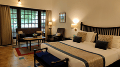 A bedroom at Jehan Numa Palace featuring a large bed with a patterned runner, warm wall-mounted lamps, and a seating area near a large window.