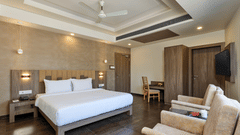 Premium Room at Pride Biznotel Sasan Gir featurinfg a double bed with nightstands on both sides and sitting space in front of it and a work desk in the background