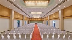 A rear view of a banquet hall with neatly arranged chairs with a carpet running down the center at Tulip Inn, Bhopal.