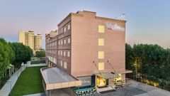 The facade of Tulip Inn, Bhopal, framed by trees on both sides and set against a backdrop of clear blue sky.