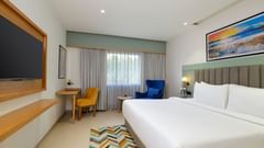 A side view of a room featuring a double bed with a television positioned in front at Tulip Inn, Bhopal.