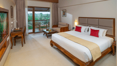 Exotica Room at Uday Suites with wooden furniture, plush bedding, warm lighting, balcony seating, and lush greenery views for a relaxing stay