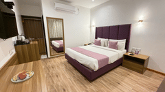 VITS Daman Devka Beach Executive Cottage with king bed, purple headboard, pink accent runner, wooden desk, mirror, and warm lighting in a bright spacious room.