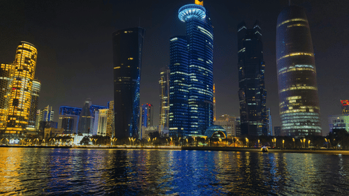 Skyline at night with illuminated skyscrapers reflecting on the water.