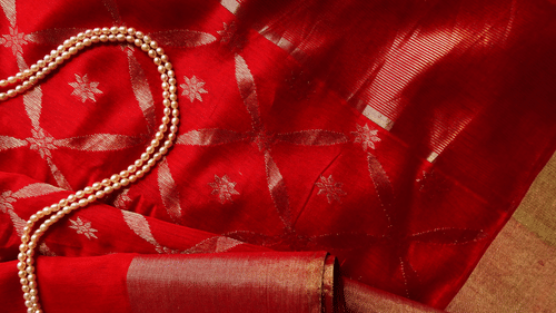 a red silk saree placed on a table with a necklace on top of it as well
