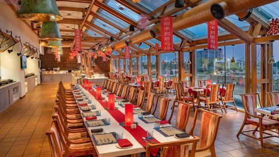Elegant dining area with a long banquet-style table, wooden chairs, and warm lighting at O by Tamara, Trivandrum.