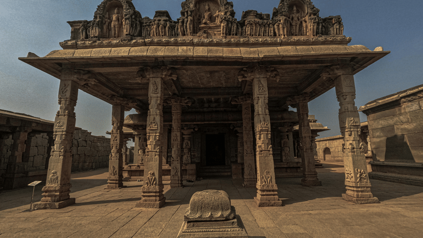 View looking into a historic temple hall with ornate stone pillars and a central altar.