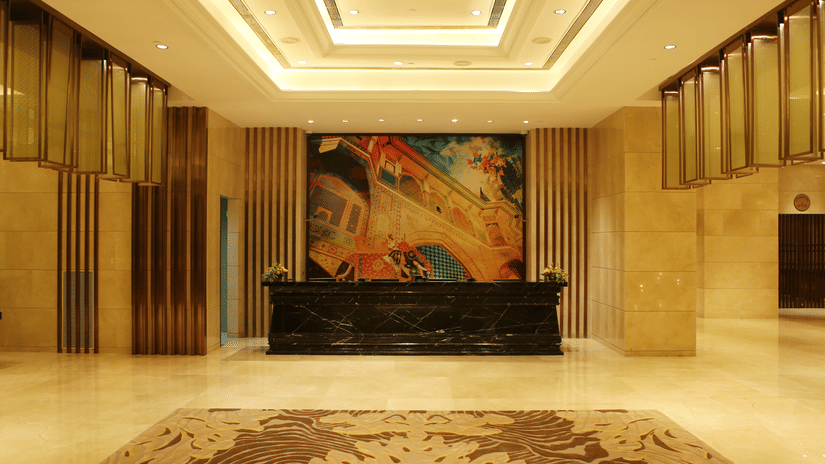 A lobby at Pride Plaza Hotel New Delhi featuring a desk and behind it  there is a huge abstract wall art. The lights and installed in the ceilings , creating a warm look.