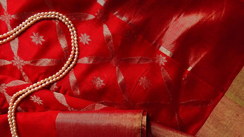 a close up image of a red saree with pearl necklace kept on top of the saree