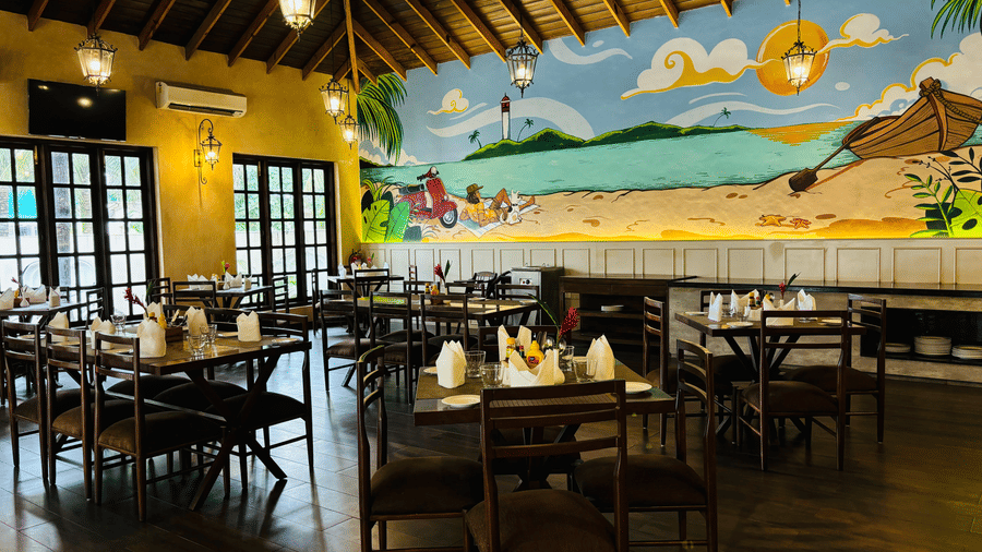 A dimly lit dining area of the Tulipe Restaurant with a wooden high ceiling, big window-style doors - Golden Tulip Goa Mandrem
