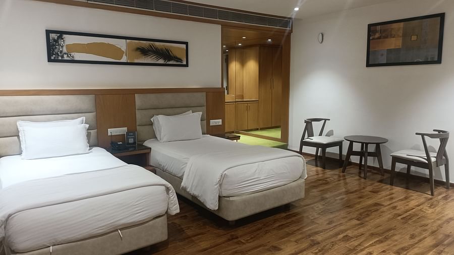 A closer perspective of the Deluxe Twin With Breakfast room at Kyriad Hotel, Gulbarga, highlighting the two beds with white linens, a decorative headboard, and two simple wooden chairs.