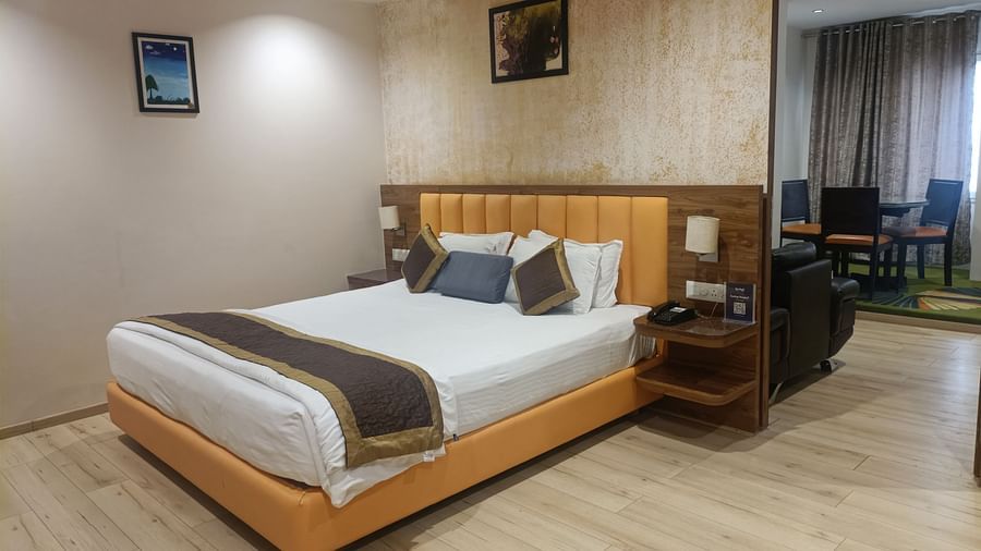 A lower corner view of the bedroom in a Junior Suite at Kyriad Hotel, Gulbarga, with a made bed, a decorative headboard, and a framed artwork on the wall.