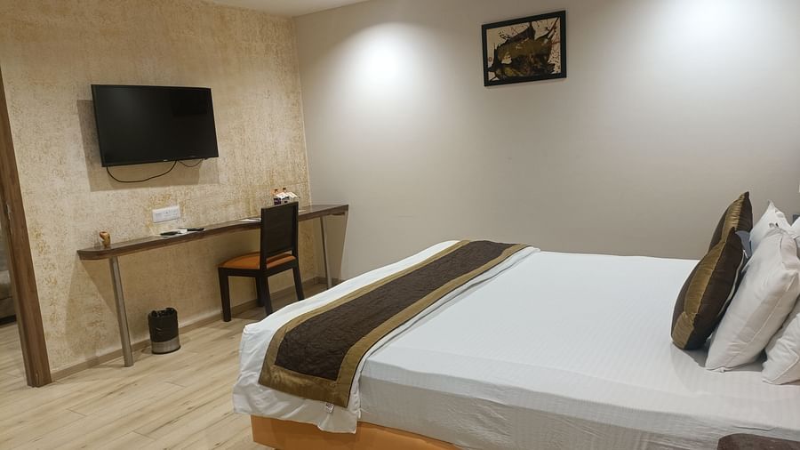 A corner view of the bedroom in a Junior Suite With Breakfast at Kyriad Hotel, Gulbarga, with a made bed, a desk area, and a framed picture on the wall.