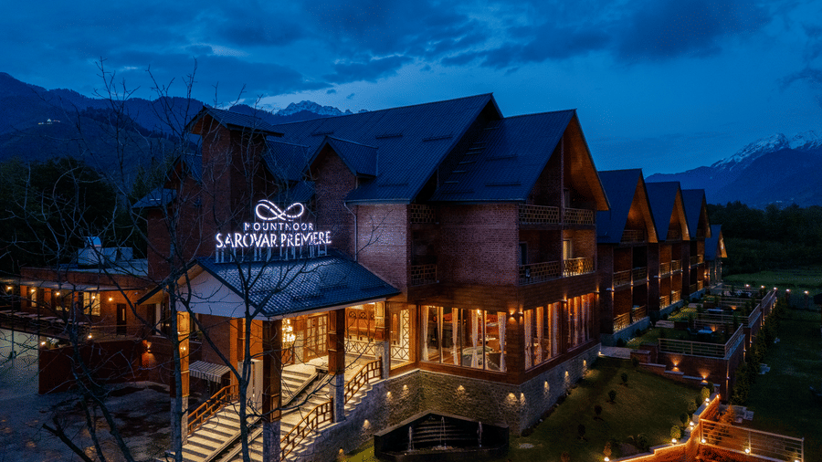 Evening view of Mountnoor Sarovar Premiere, Pahalgam illuminated against the scenic Himalayan landscape under a dramatic sky.
