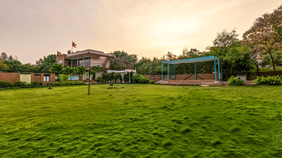 Expansive manicured green lawn at the resort during sunset, surrounded by trees - Nature Trails Ashoka Resort Hampi