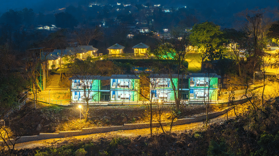 Alt Text: Aerial night view of Nature Trails Durshet resort glowing with warm lights nestled among lush hills and trees.