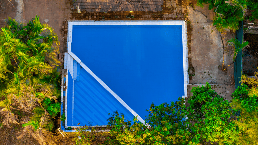 Top aerial view of the swimming pool at Nature Trails Durshet surrounded by dense greenery, palm trees, and natural landscapes.