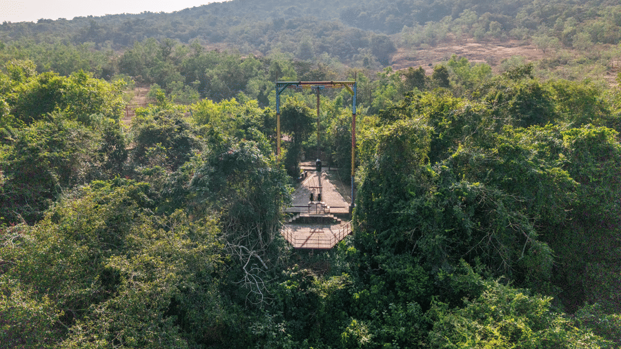 A view looking down at a tall metal structure hidden amongst green trees.