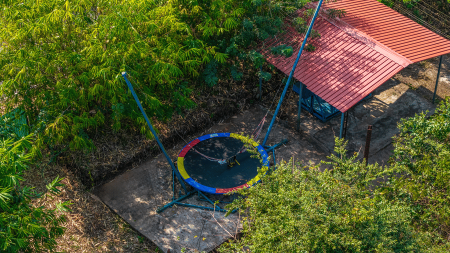 A trampoline and play equipment set up in a garden surrounded by trees.