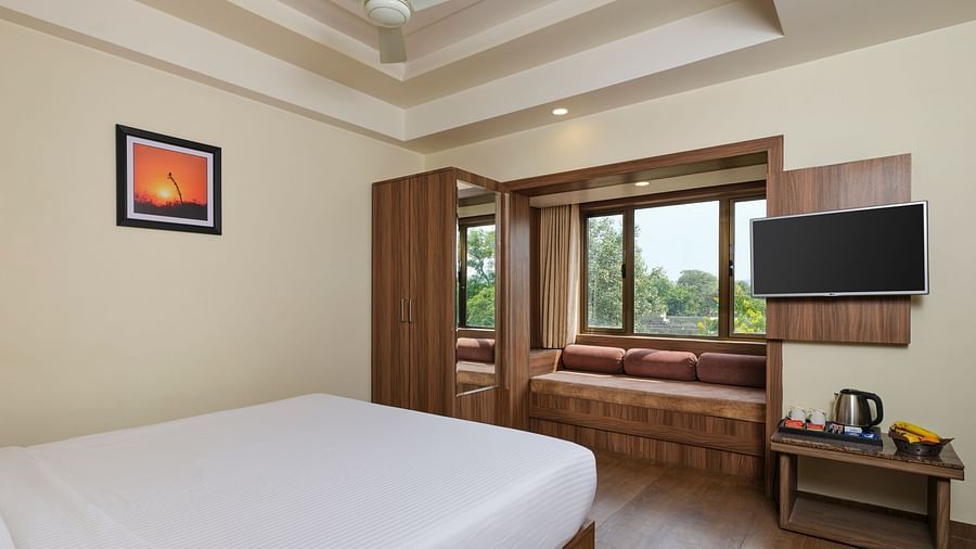 Super Desluxe Room at Pride Biznotel in Sasan Gir featuring a bed facing the TV mounted on the wall and a large window with panes made as sitting space next to it