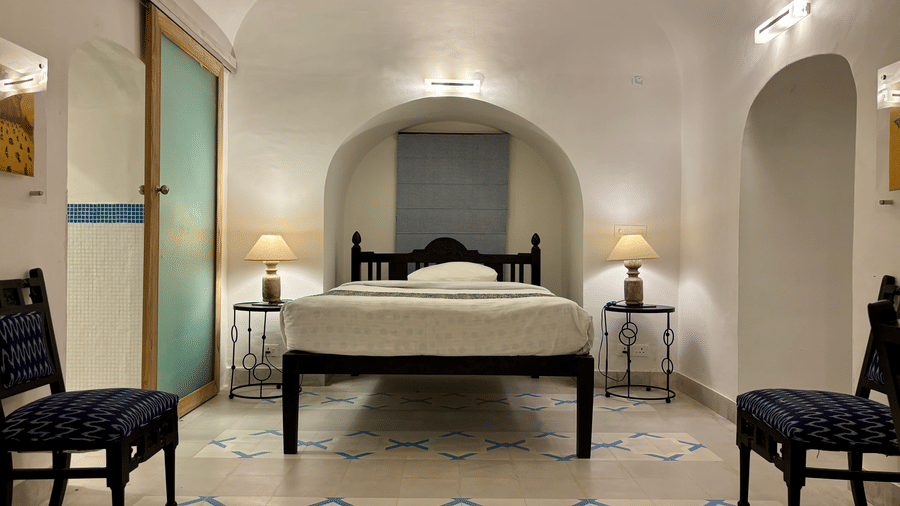 A cosy bedroom at Tijara Fort-Palace - 19th Century, Alwar, featuring an arched bed alcove and dark accent chairs.