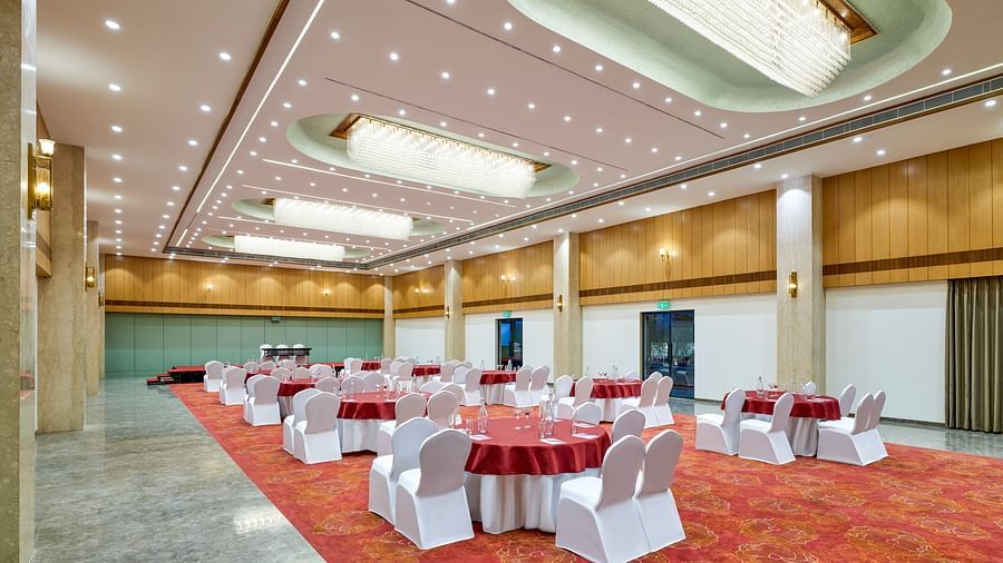 An image of a banquet hall at Tulip Inn, Bhopal, showcasing tables, chairs, and ceiling lighting.