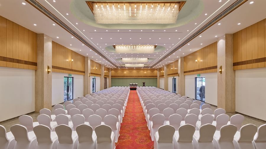 A rear view of a banquet hall with neatly arranged chairs with a carpet running down the center at Tulip Inn, Bhopal.