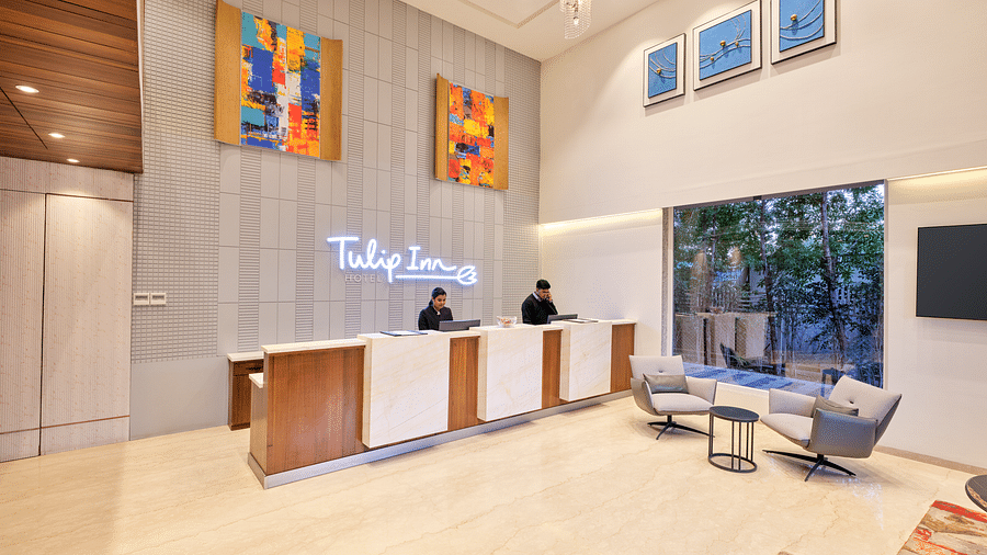 An image of a lobby featuring a reception desk with two individuals standing behind it at  Tulip Inn, Bhopal.
