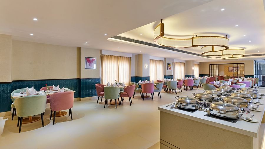An image of a dining space at Tulip Inn, Bhopal, featuring a seating area on one side and a buffet table on the other side.