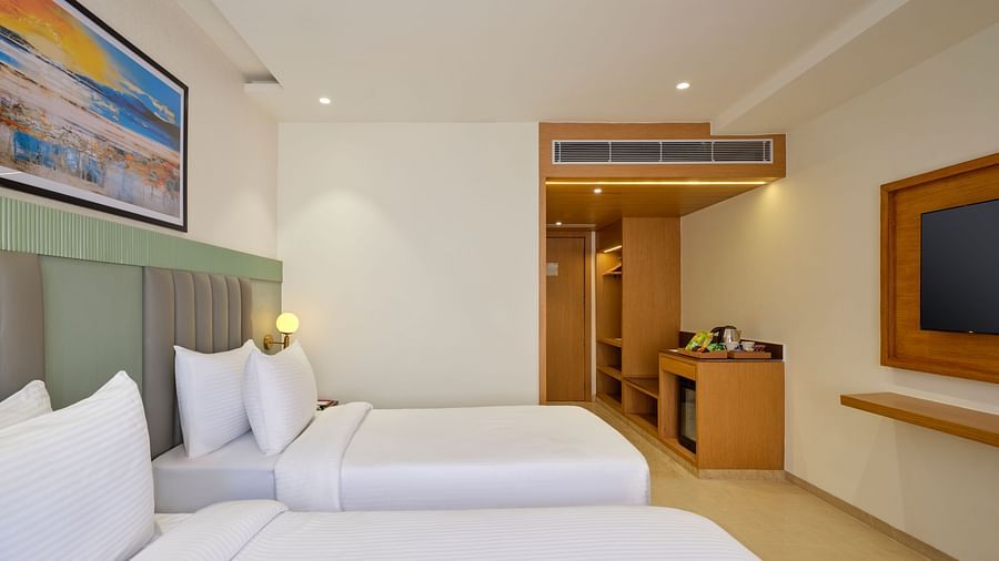 Side view of a room with twin beds and a television in front at Tulip Inn, Bhopal.