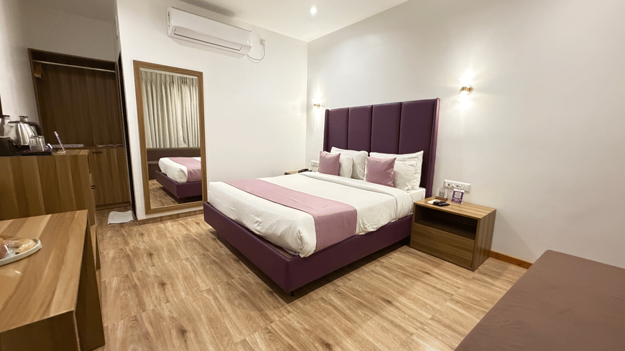 VITS Daman Devka Beach Executive Cottage interior with king-size bed, purple upholstered headboard, pink accent, wooden floor, and wardrobe in background.