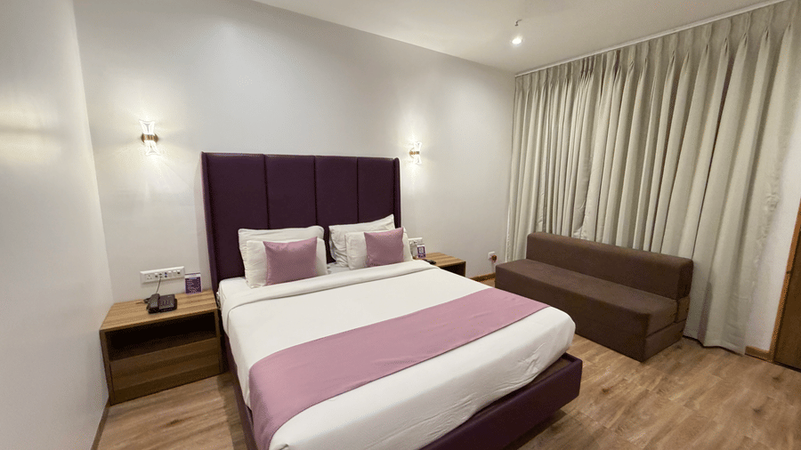 Executive Cottage at VITS Daman Devka Beach with king bed, purple headboard, pink throw, sofa chair, wooden side tables, and warm ambient lighting.