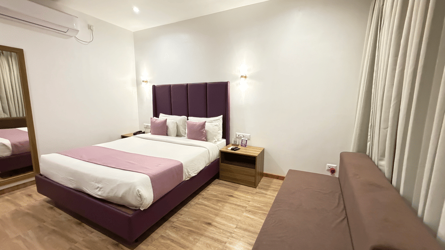 Executive Cottage at VITS Daman Devka Beach with king bed, purple tufted headboard, pink accent pillow, sofa chair, and wooden side tables.