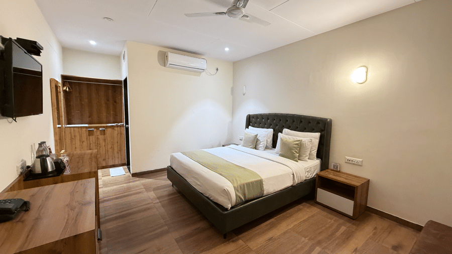 Modern cottage-style hotel room with a spacious bed and warm wooden accents and a tv mounted on wall at VITS Daman Devka Beach.
