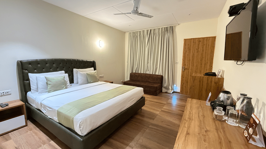 Modern cottage-style hotel room featuring a spacious bed, warm wooden accents, and a wall-mounted TV at VITS Daman Devka Beach.
