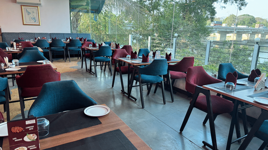 An overview of the seating arrangement at Riverside Restaurant, one of the best restaurants in Silvassa, with a large floor to ceiling window having lake views at at VITS Kamats Resort, Silvassa.