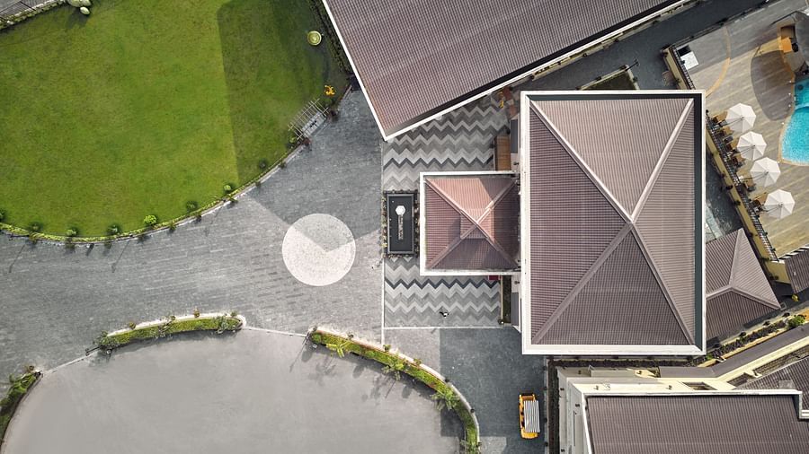 Aerial view of a modern resort with geometric rooftops, a circular driveway, a green lawn, and a swimming pool with poolside umbrellas - Voyage The Solitaire Bliss.