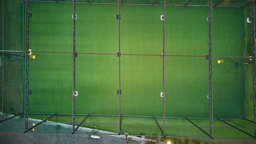 Aerial view of an enclosed green cricket turf field with overhead netting, lighting fixtures, and clear boundary lines - Voyage The Solitaire Bliss.