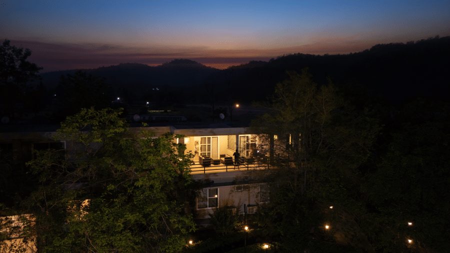 Resort building with lights on, set against a backdrop of hills and a twilight sky
