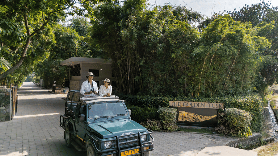 An open vehicle driving along a paved path with people seated inside and greenery on both sides.