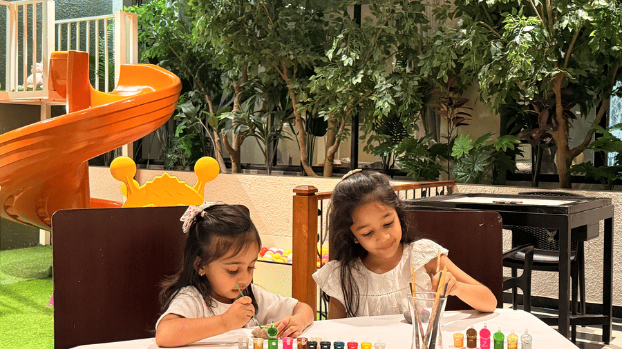 Two young girls sitting at a table outdoors, coloring with crayons and paints at The Golden Tusk, Jim Corbett